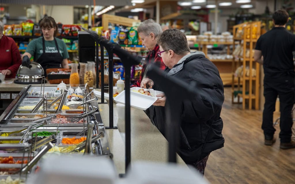 Customers selecting food from supermarket buffet.