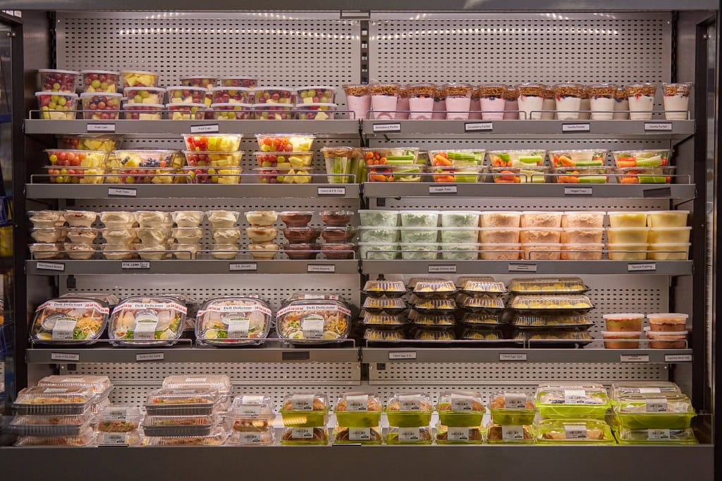 Refrigerated shelf with assorted pre-packaged healthy snacks.